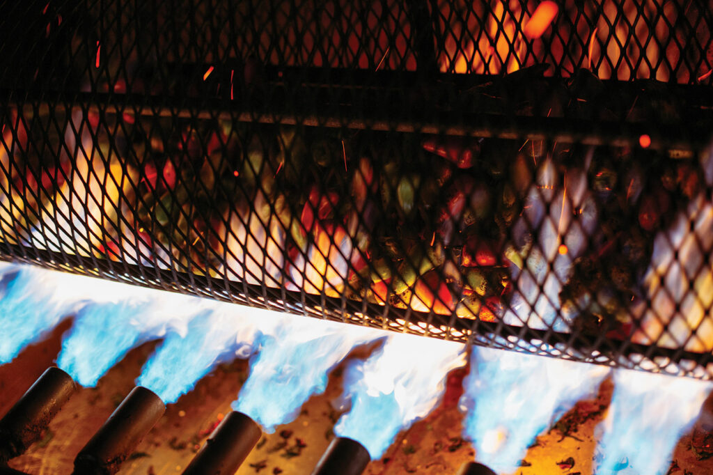 Chiles in a metal cage being hit with jets of blue flame.