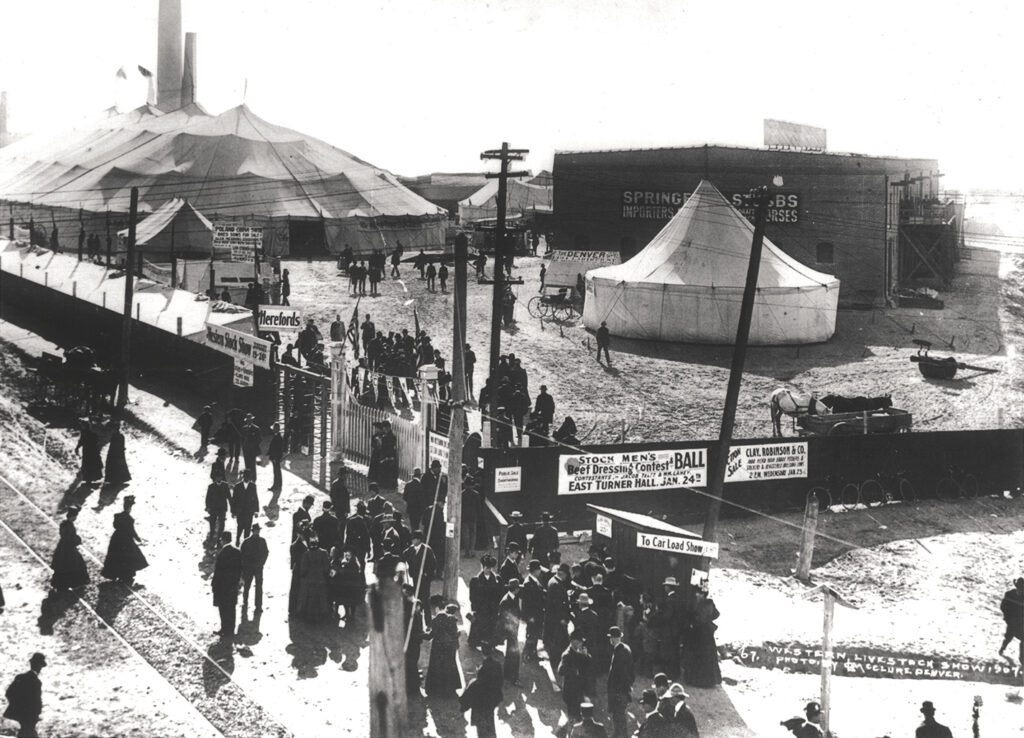 Black and white photo of big tents with people standing outside.