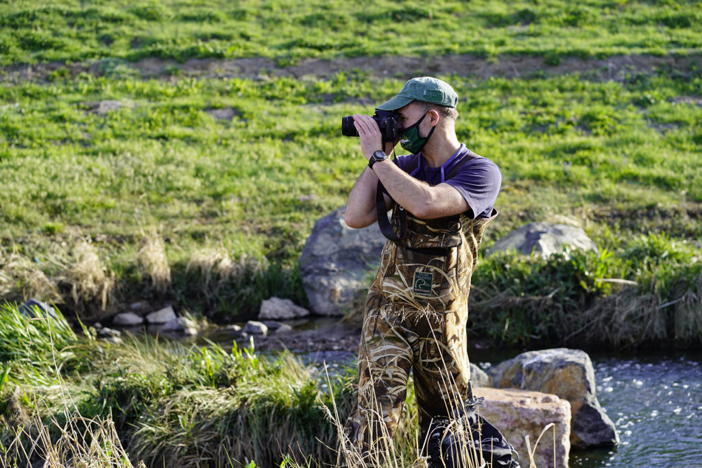 A man standing in a river looks through binoculars.