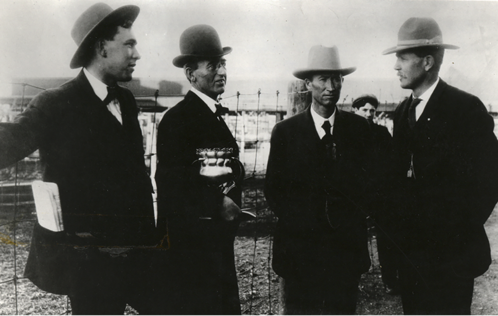 Black and white photo of four people in suits and hats.