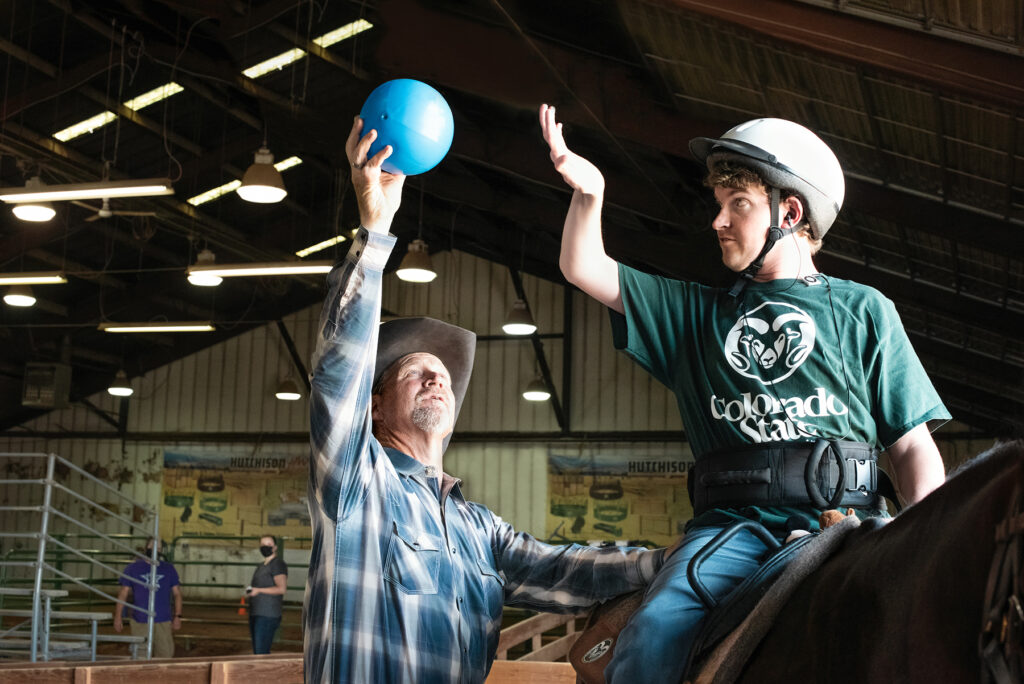 A man holds up a blue ball next to a boy on a horse.