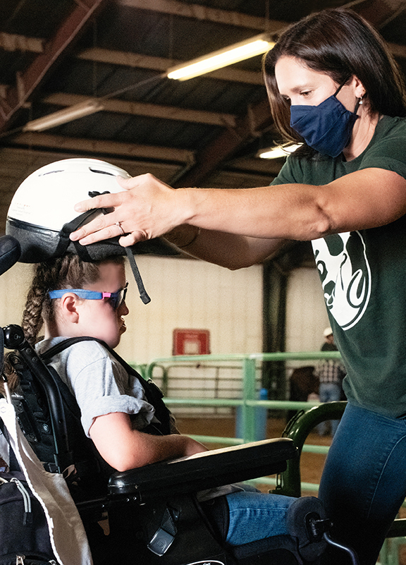 A woman puts a white helmet on a girl.
