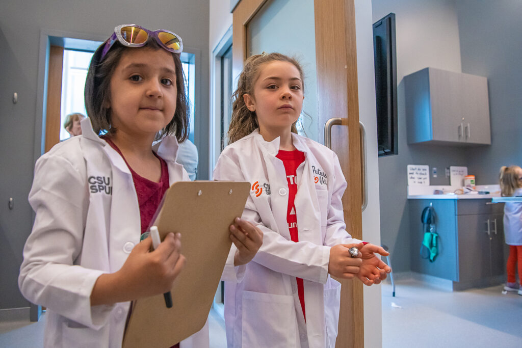 Two kids wear lab coats and hold clip boards.