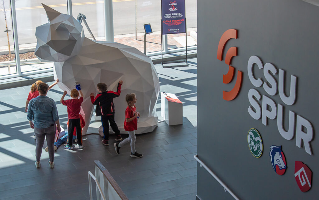 As seen from above, kids cluster around a large white cat statue with the CSU Spur logo in the foreground.