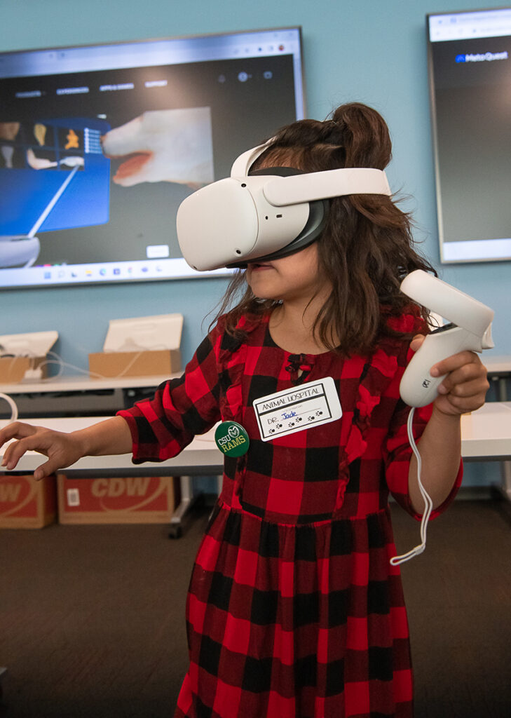 A child in a red and black plaid outfit wears a virtual reality headset.