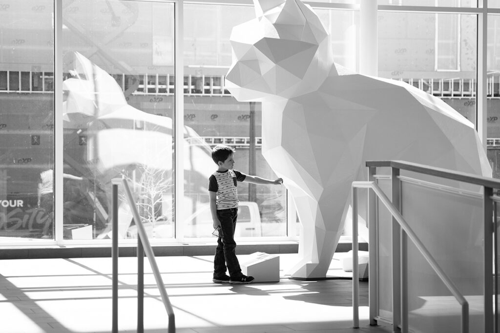 A boy stands in front of a large white cat statue.