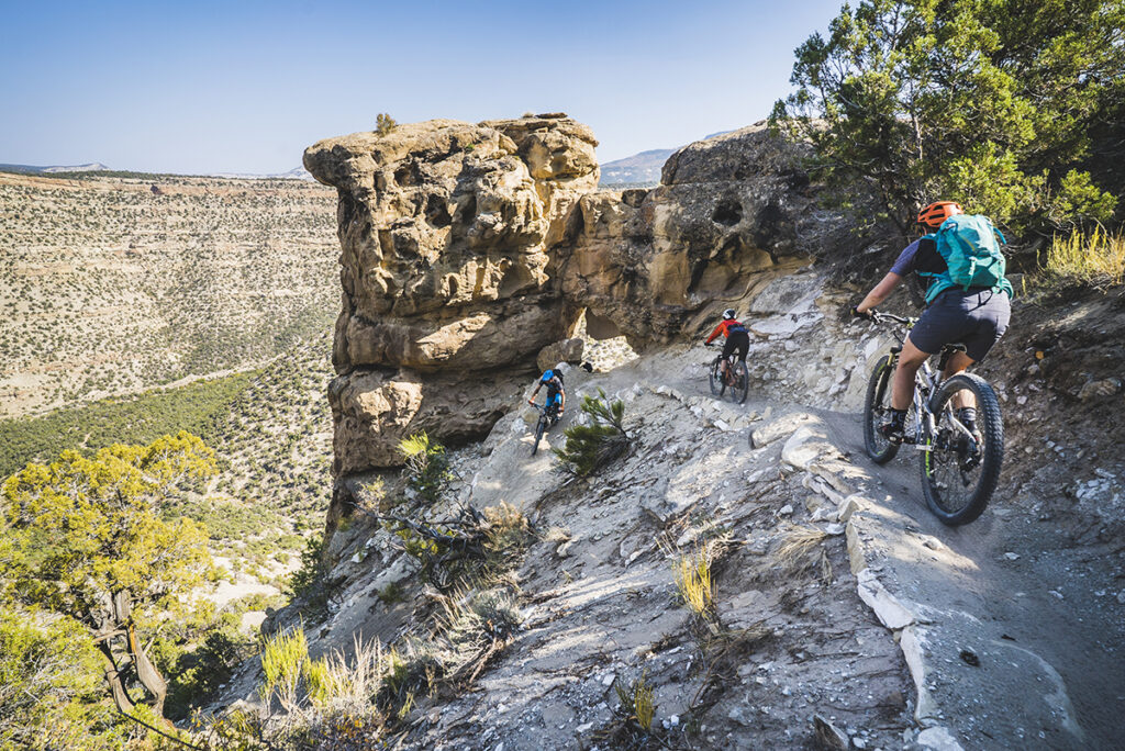 Mountain bikers on a path that follows the side of a cliff.