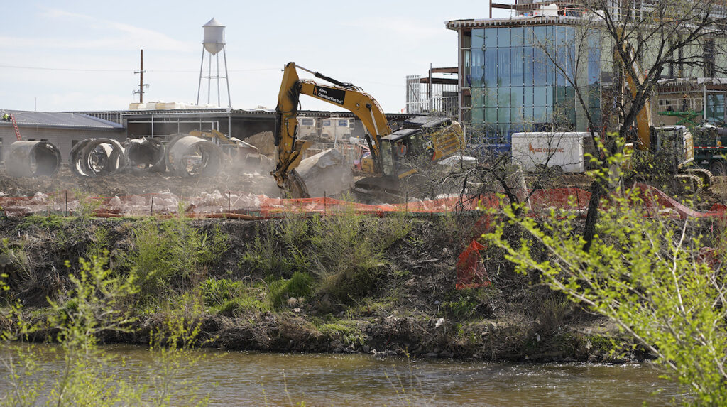 A backhoe digs on the bank of a river.