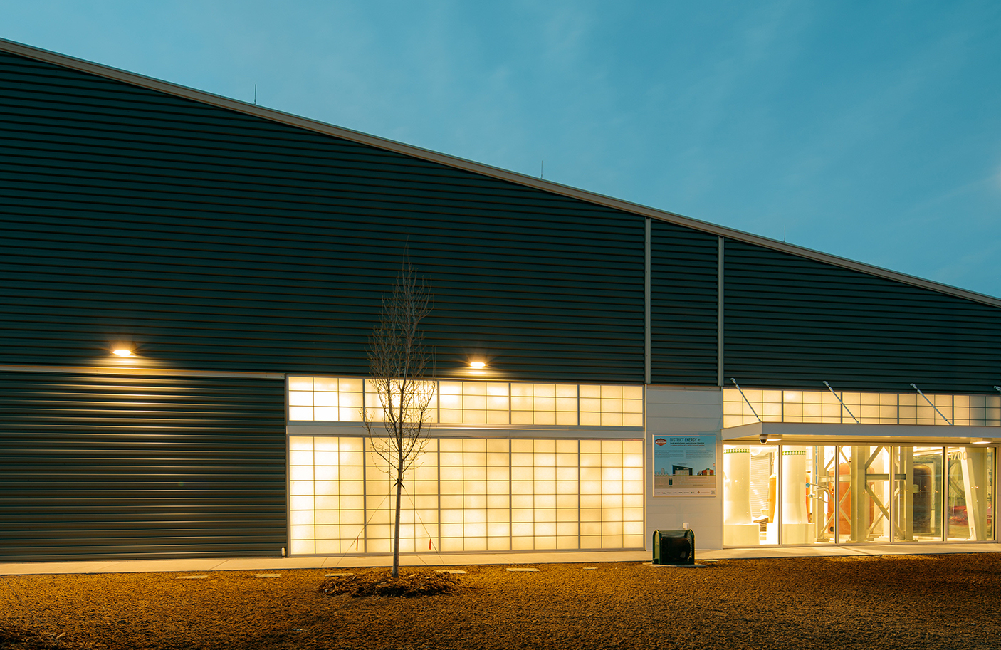 Building with a slanted roof and light on through the windows.