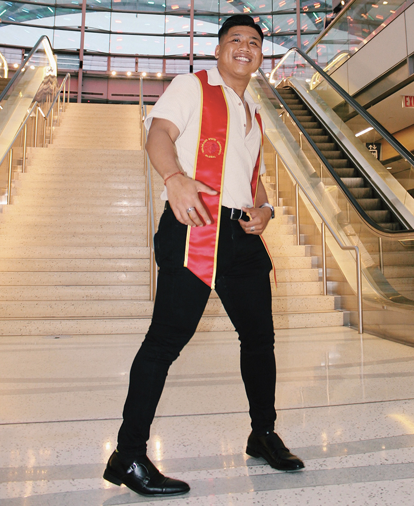 A man in a graduation sash stands on a staircase.