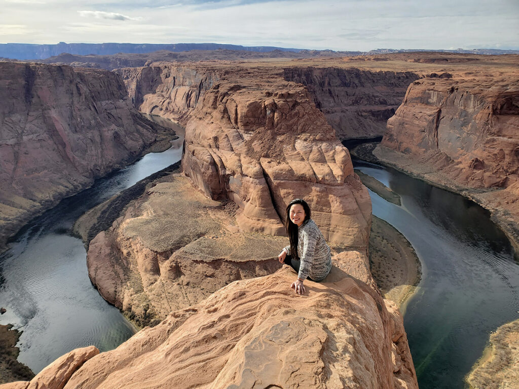 Woman sits on a rock overlooking a deep river bend.