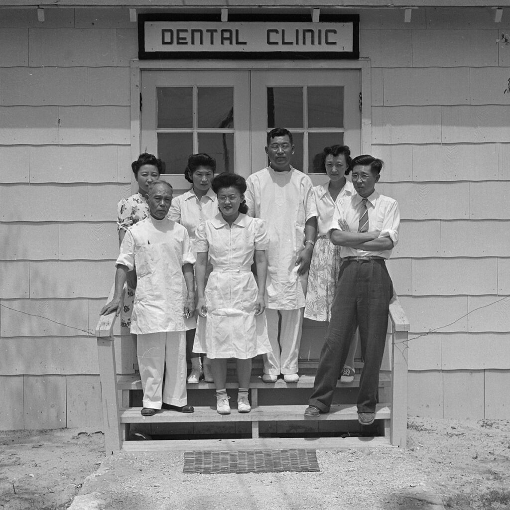Black and white photo of a group standing in front of building labeled Dentist Clinic.