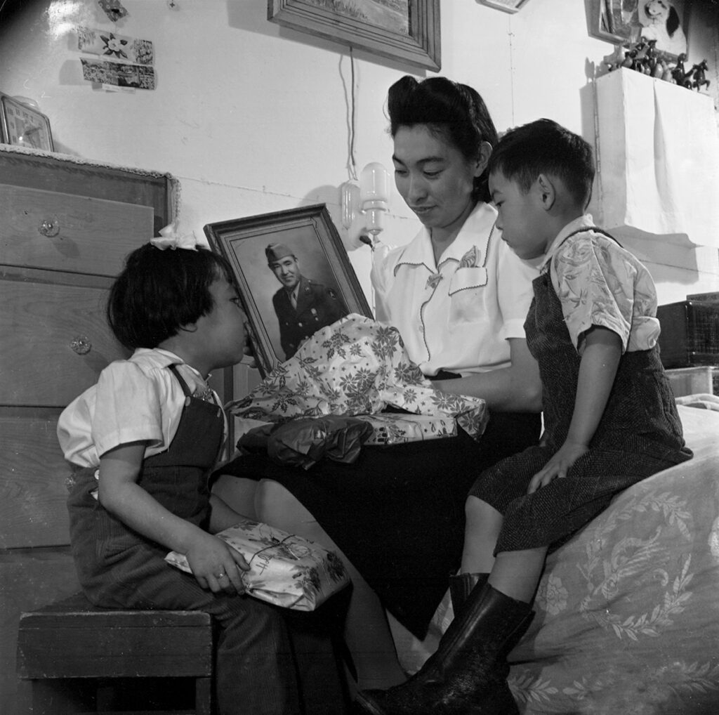 Black and white photo of a mother showing a framed photo to two children.