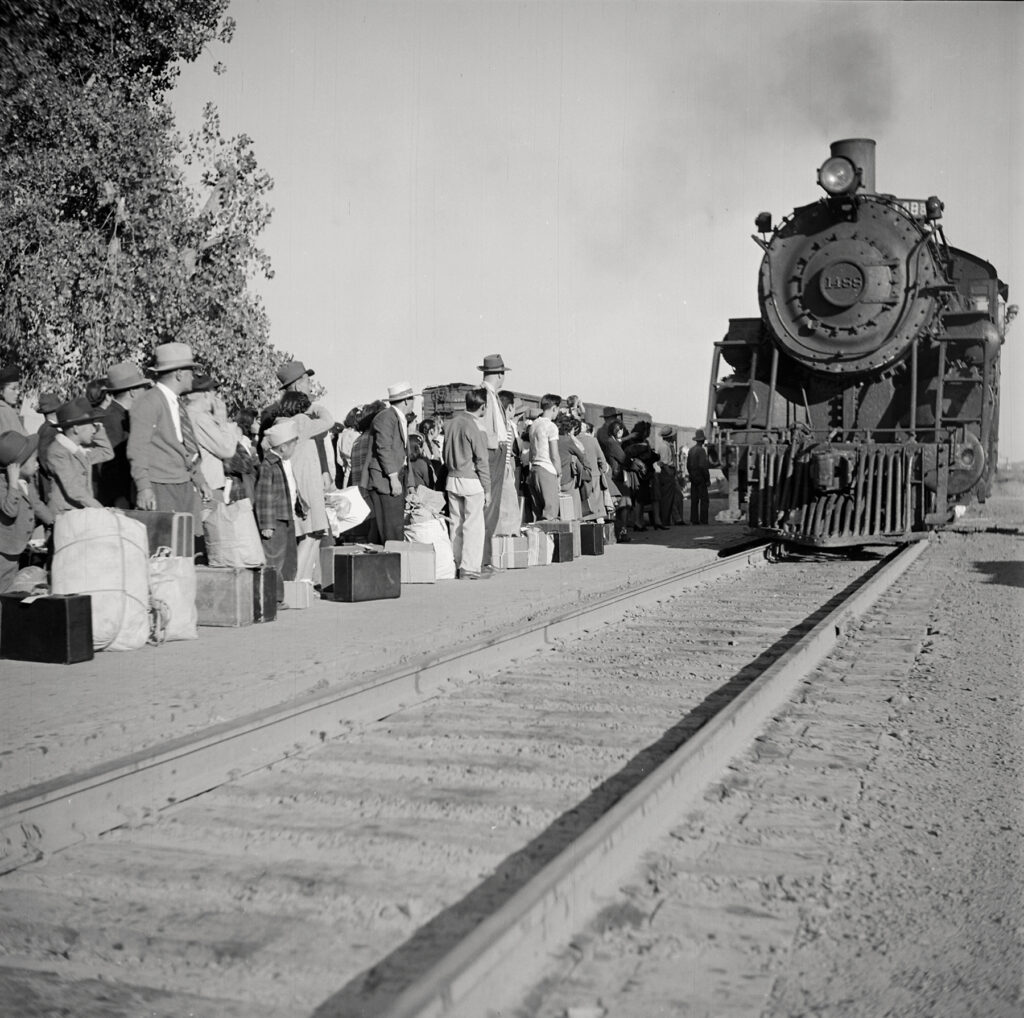 Black and white photo of a train pulling up to a platform with a crowd on it.