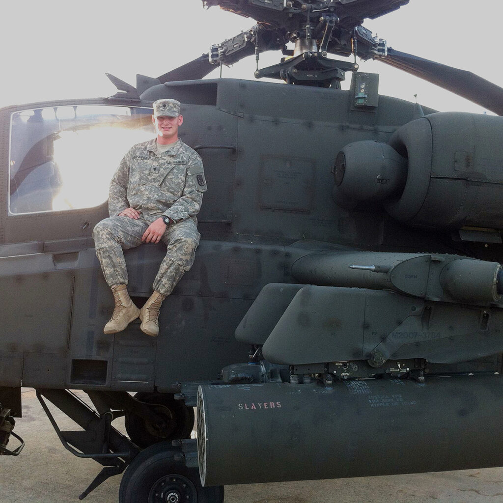 Man in military fatigues sitting on a helicopter.