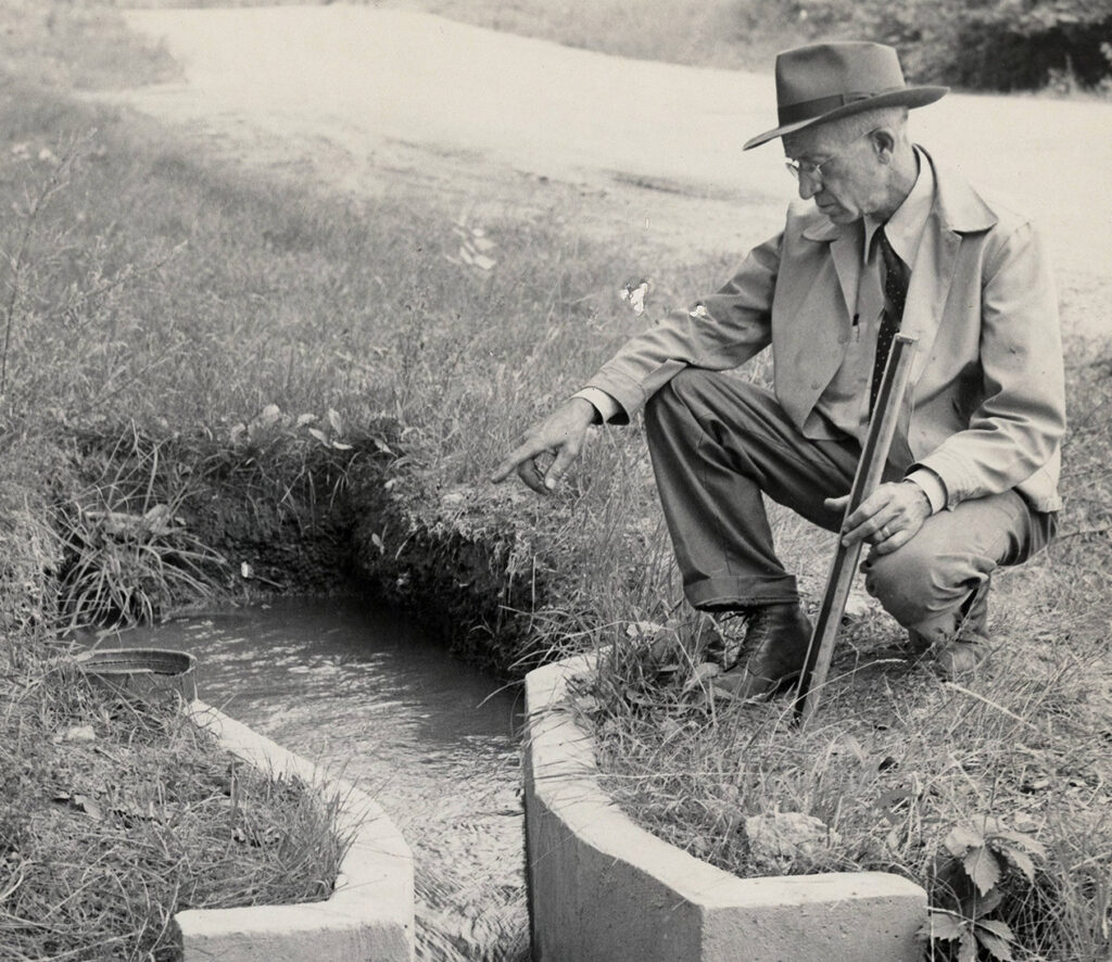 Historic photo of a man crouching by an irrigation ditch.