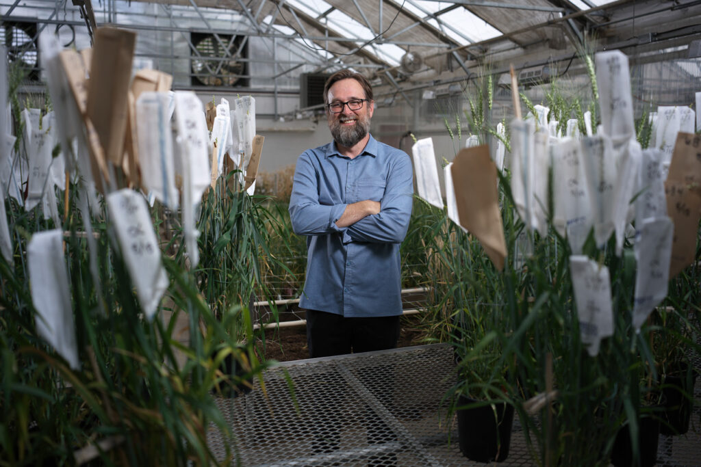 A man stands in a greenhouse amid a lot of labeled plants.
