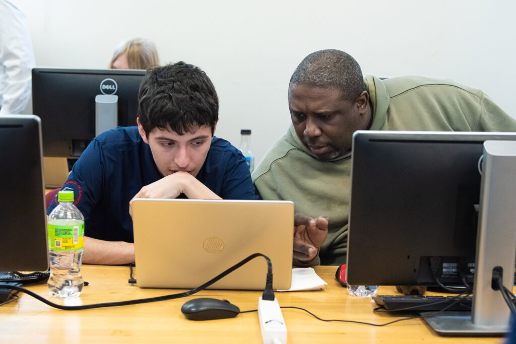 Two people look at a laptop screen.