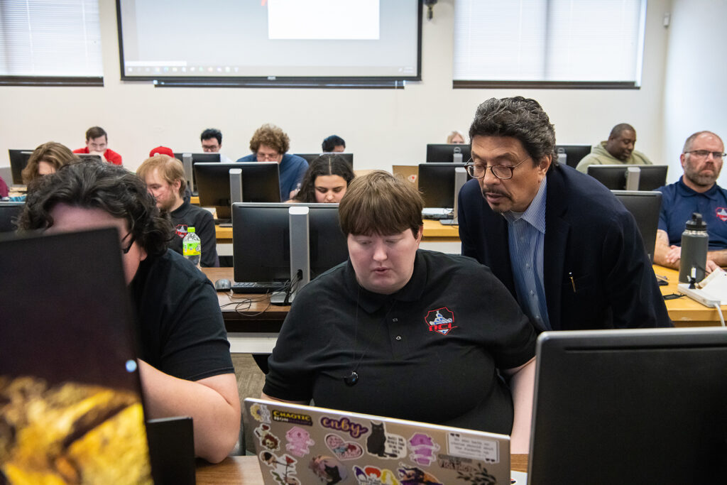 A person looks over a student's shoulder at a laptop screen.