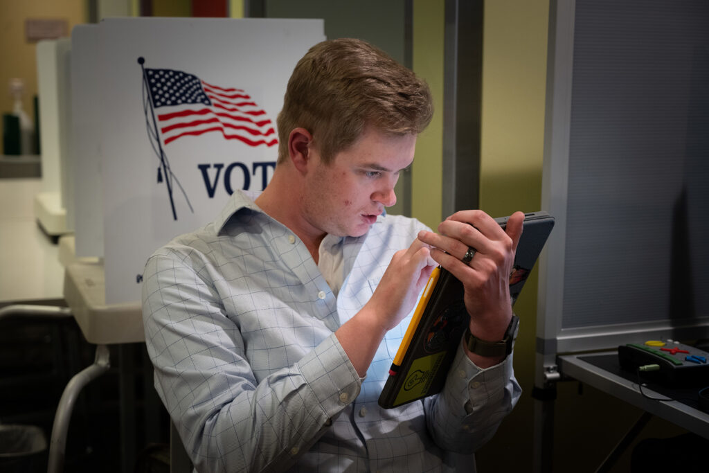 A man reads a book in front of a voting sign.