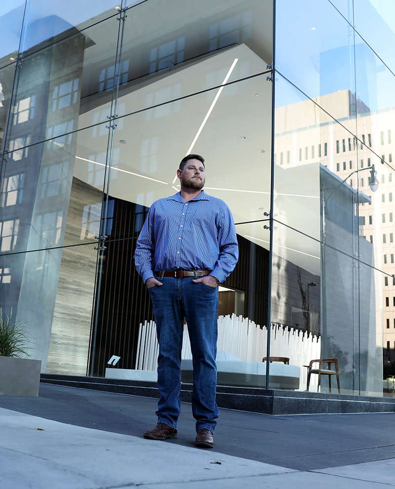 A man poses in front of bank of windows in a downtown landscape.