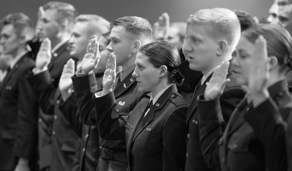 Black and white photo of people in military dress with one hand raised.