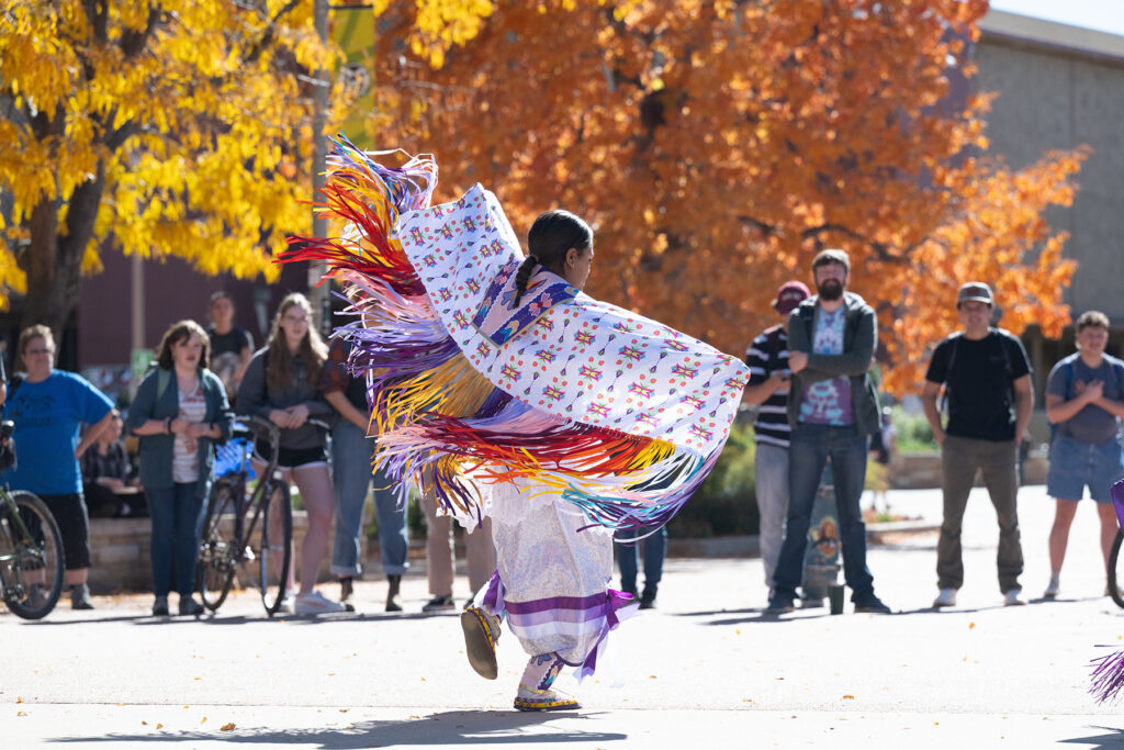 A person in Native American dress dances on a plaza.