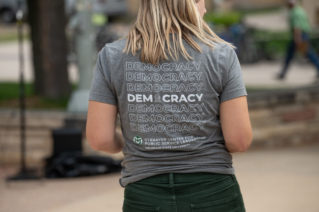 The back of a gray shirt that says "democracy" in several rows.