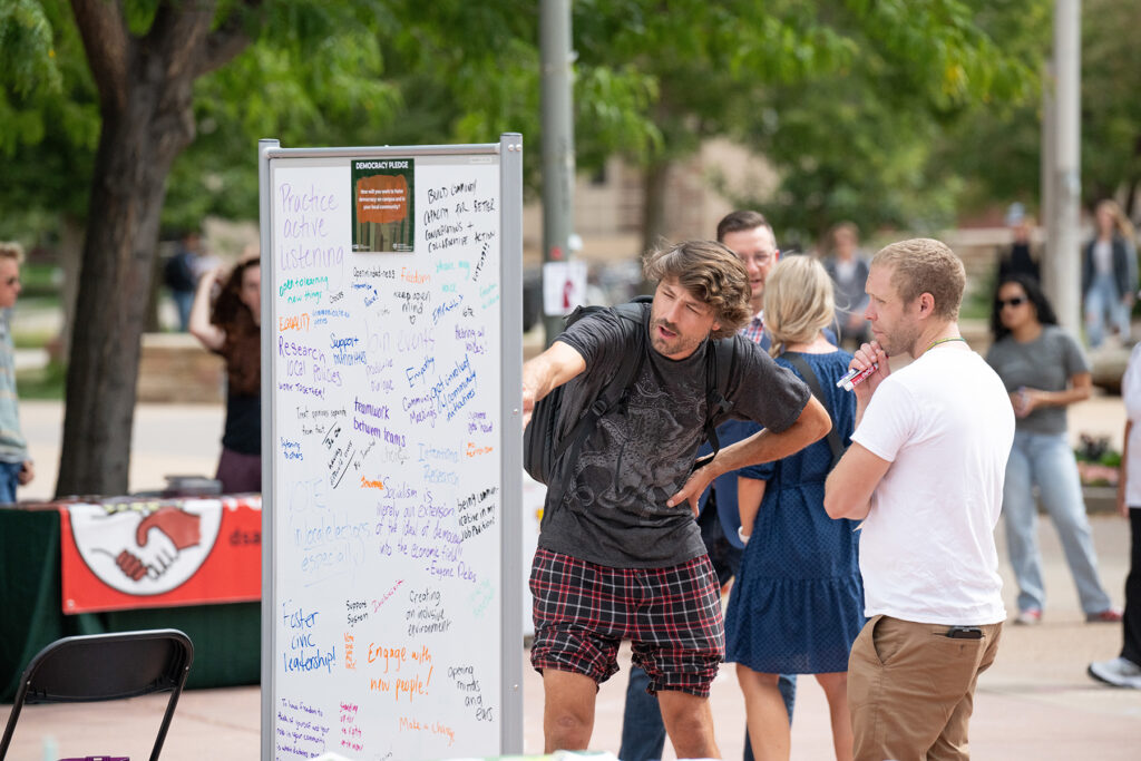 Two people look at a white board on a plaza.