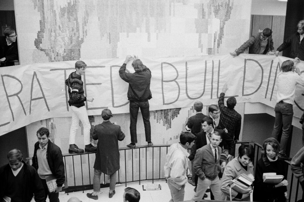 Black and white photo of students hanging a handwritten banner on a wall.