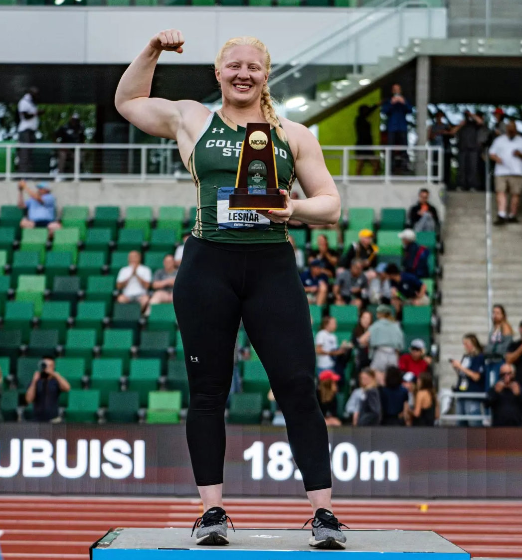 A woman flexes on a podium holding a trophy.