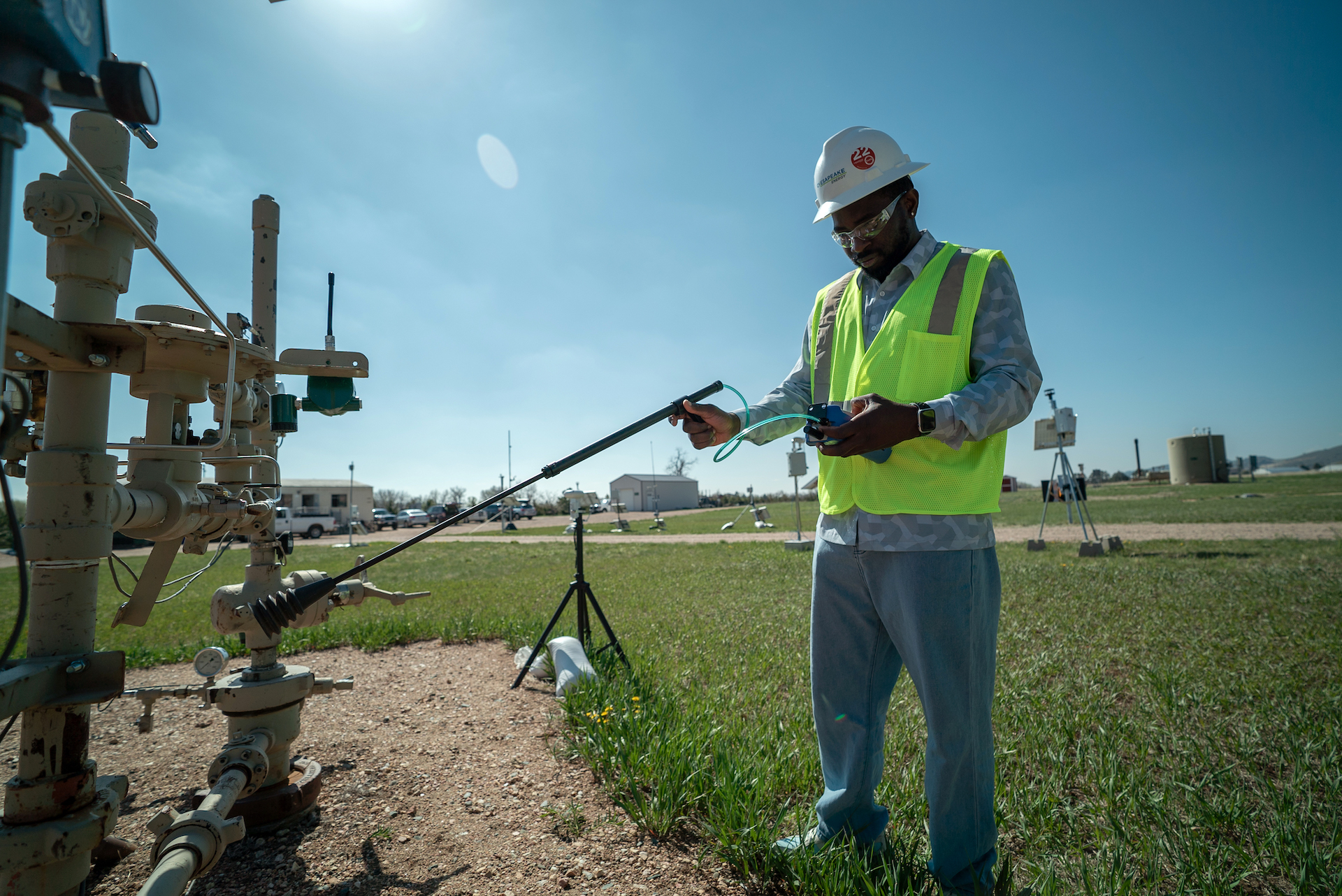 A student in a hard hat and reflective vest uses a long tool to take measurements.