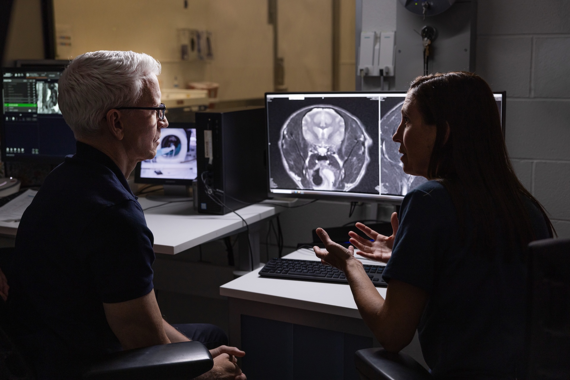 A man and woman talk in front of a computer screen displaying a medical image.