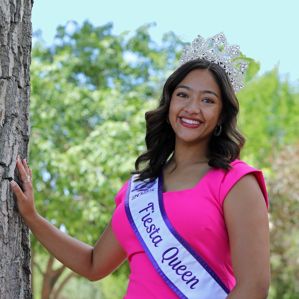 A woman in a pink dress and tiara with a crossbody sash that reads Fiesta Queen.