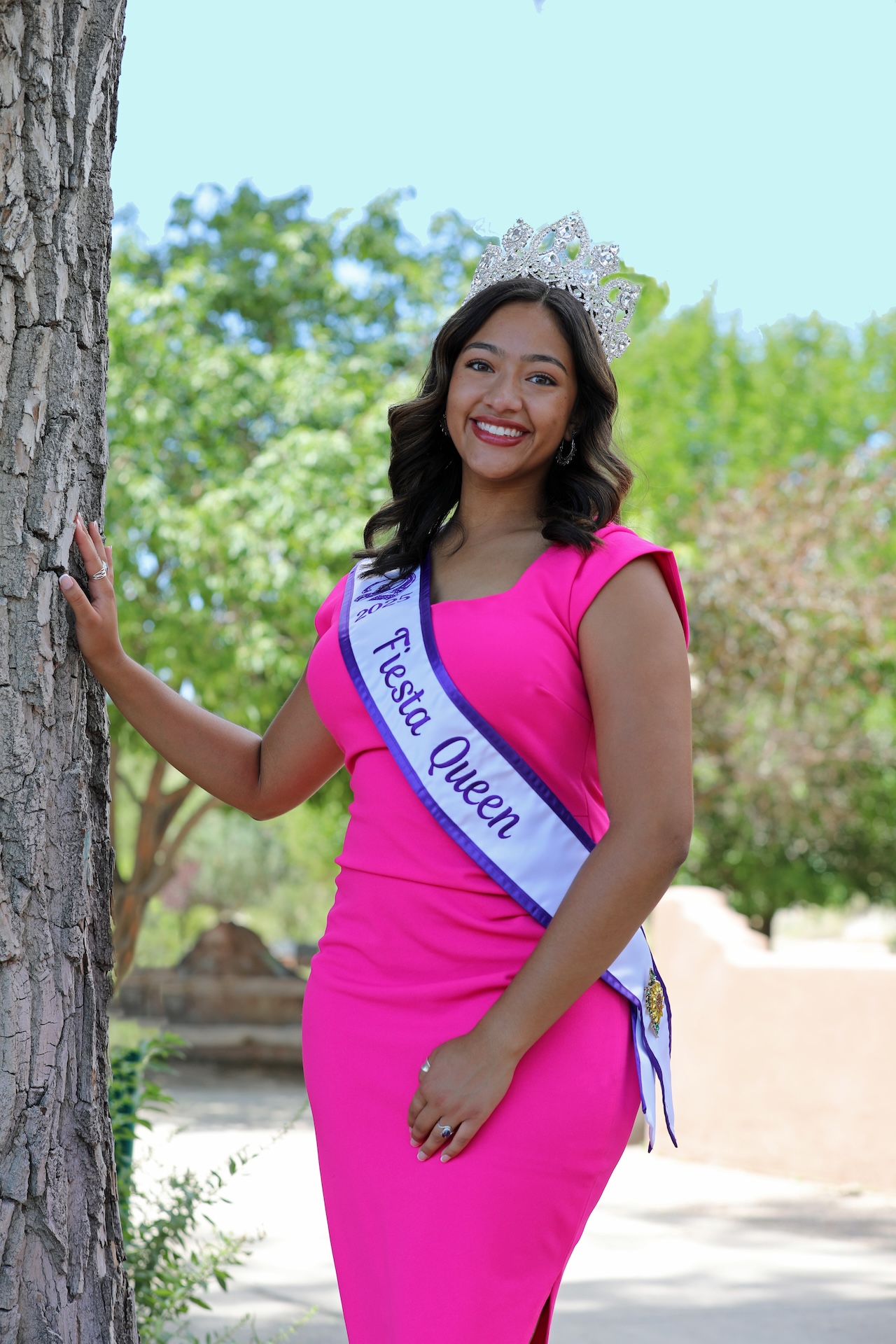 A woman in a pink dress and tiara with a crossbody sash that reads Fiesta Queen.
