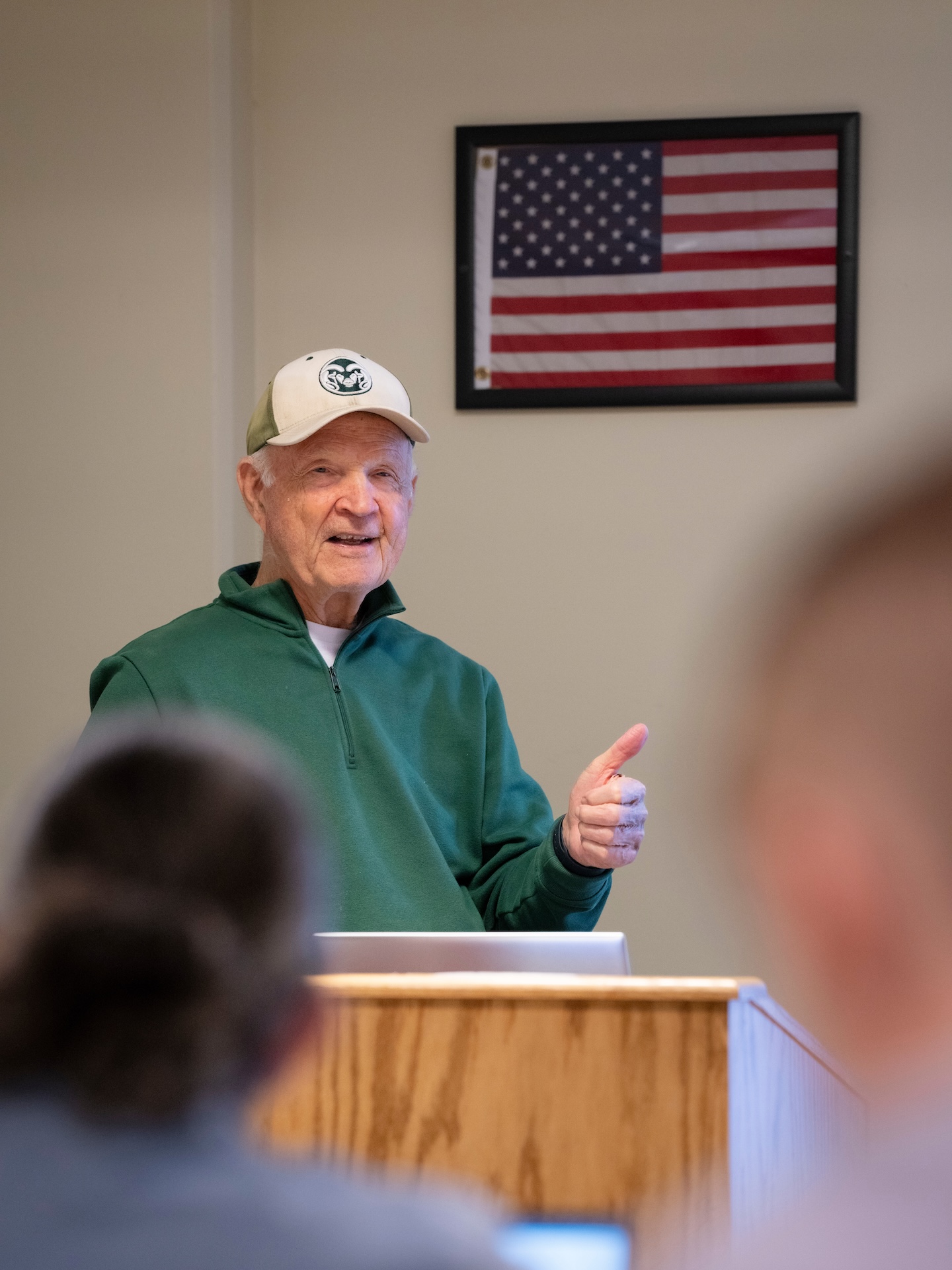 A man in a hat and a green sweater stands at a podium.