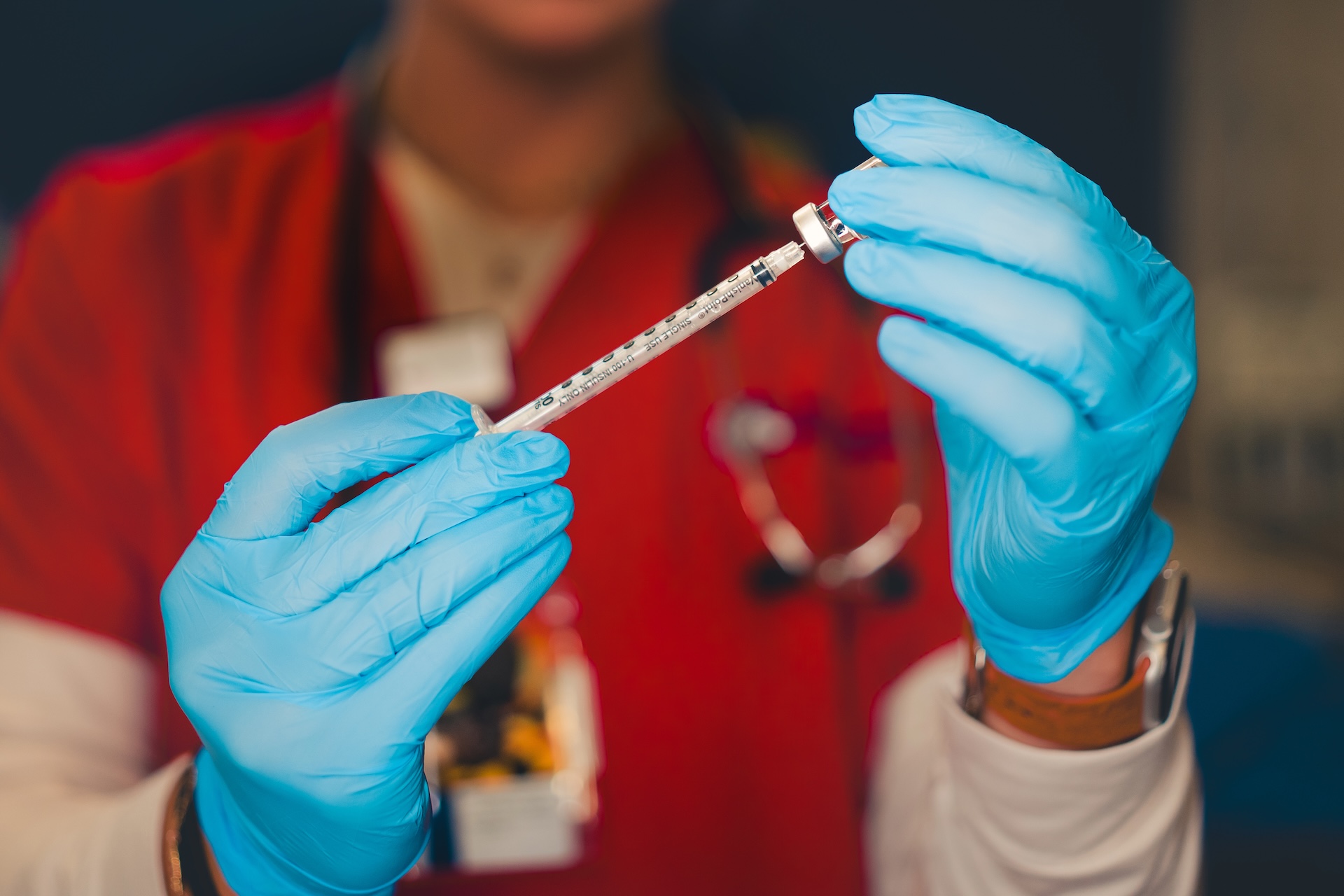A person wearing blue gloves holds a syringe.