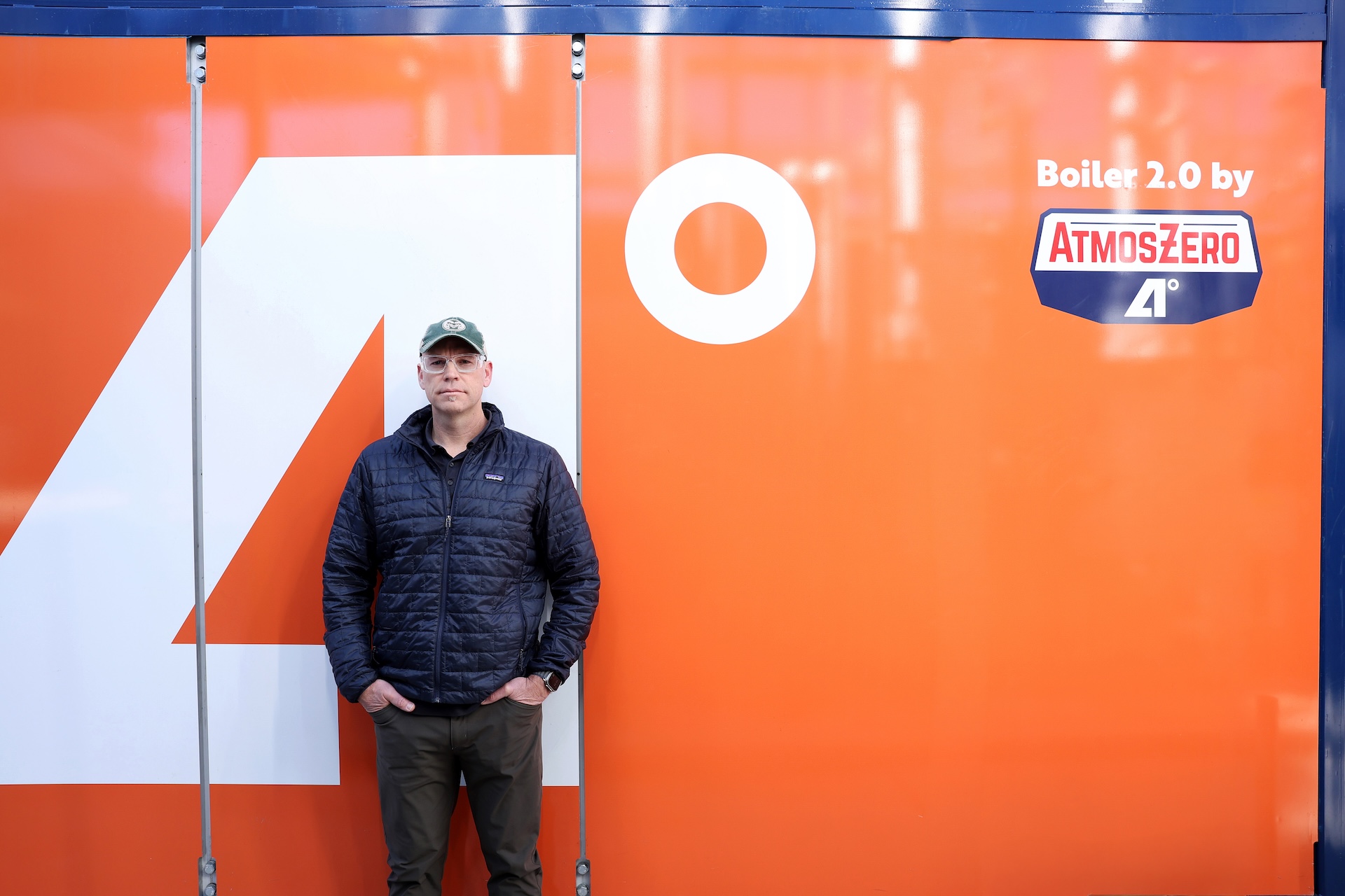 A man poses in front of an orange machine with an AtmosZero logo.