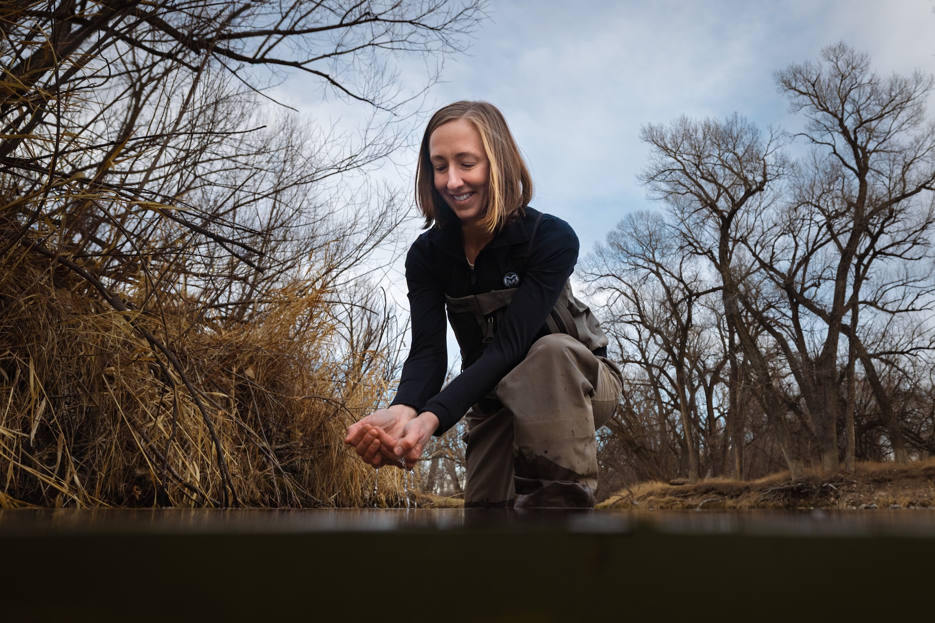 A woman crouches in a river with water cupped in her hands.